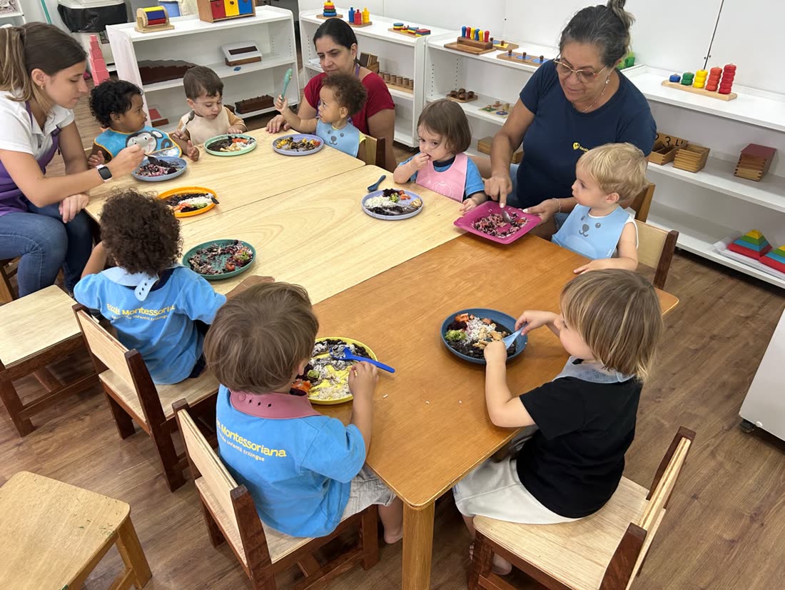 Jeunes enfants déjeunant ensemble à la table basse de l'ambiance, chacun avec son assiette, deux éducatrices tout près