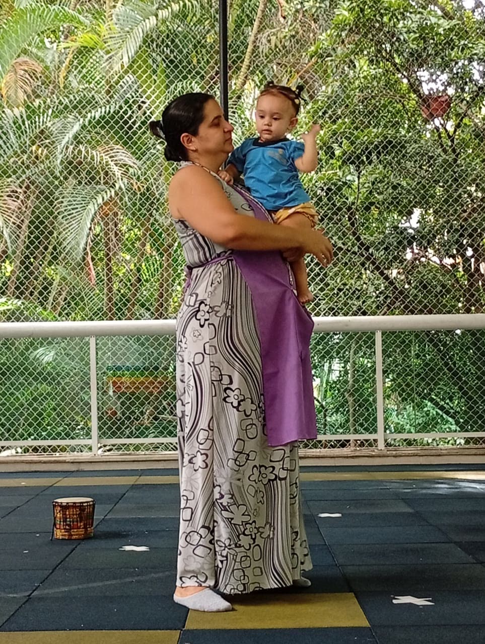 Professora com bebê no colo no pátio arborizado da escola