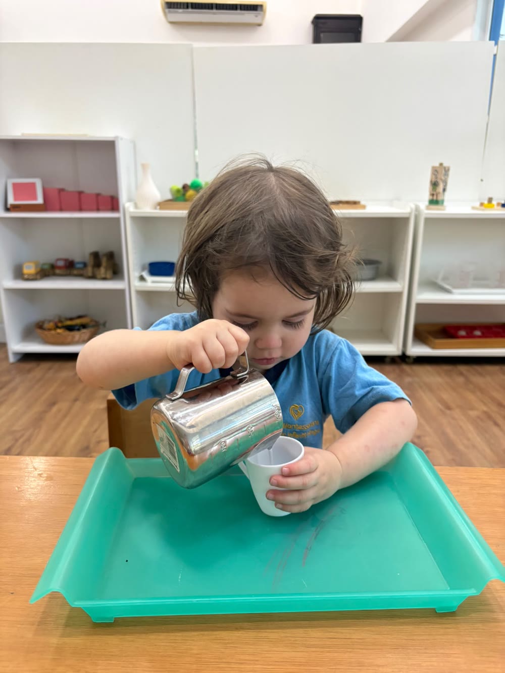 Petite fille concentrée versant de l'eau d'un pichet dans l'ambiance, les étagères en arrière-plan