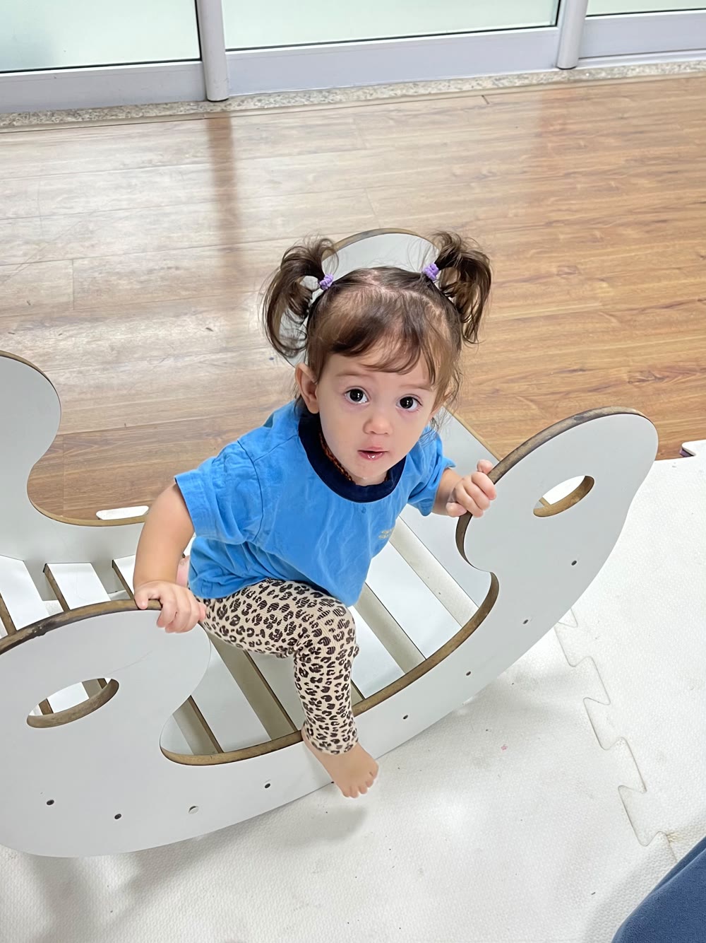 Menina pequena subindo no balanço-arco de madeira, dentro da sala