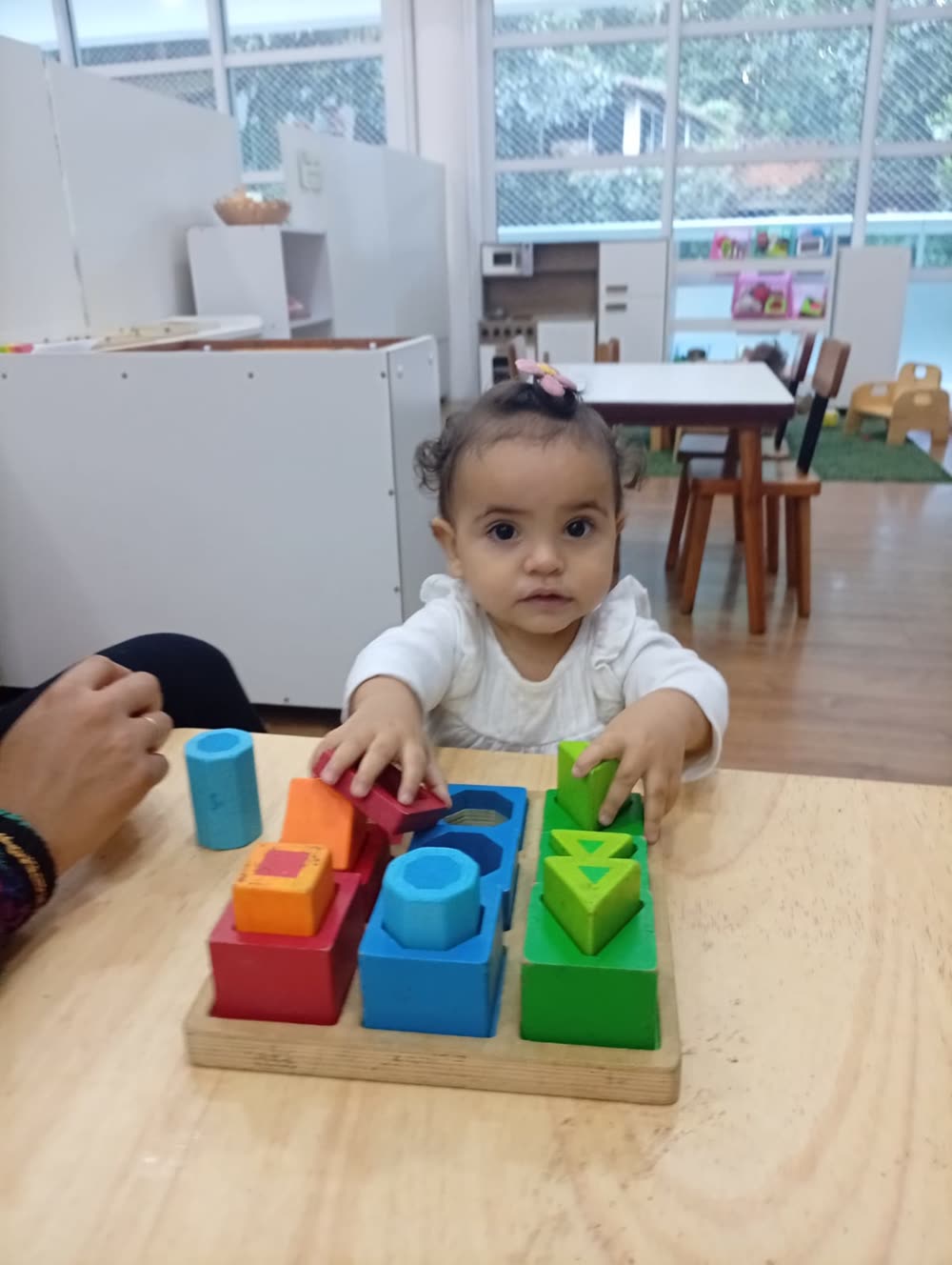 Bebê encaixando blocos geométricos coloridos na base de madeira, com concentração