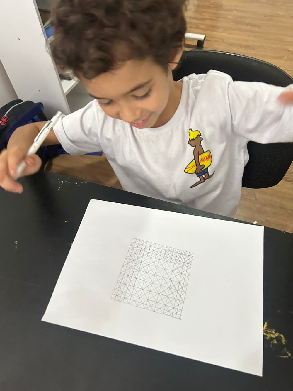 Aluno do Fundamental desenhando com lápis sobre malha quadriculada