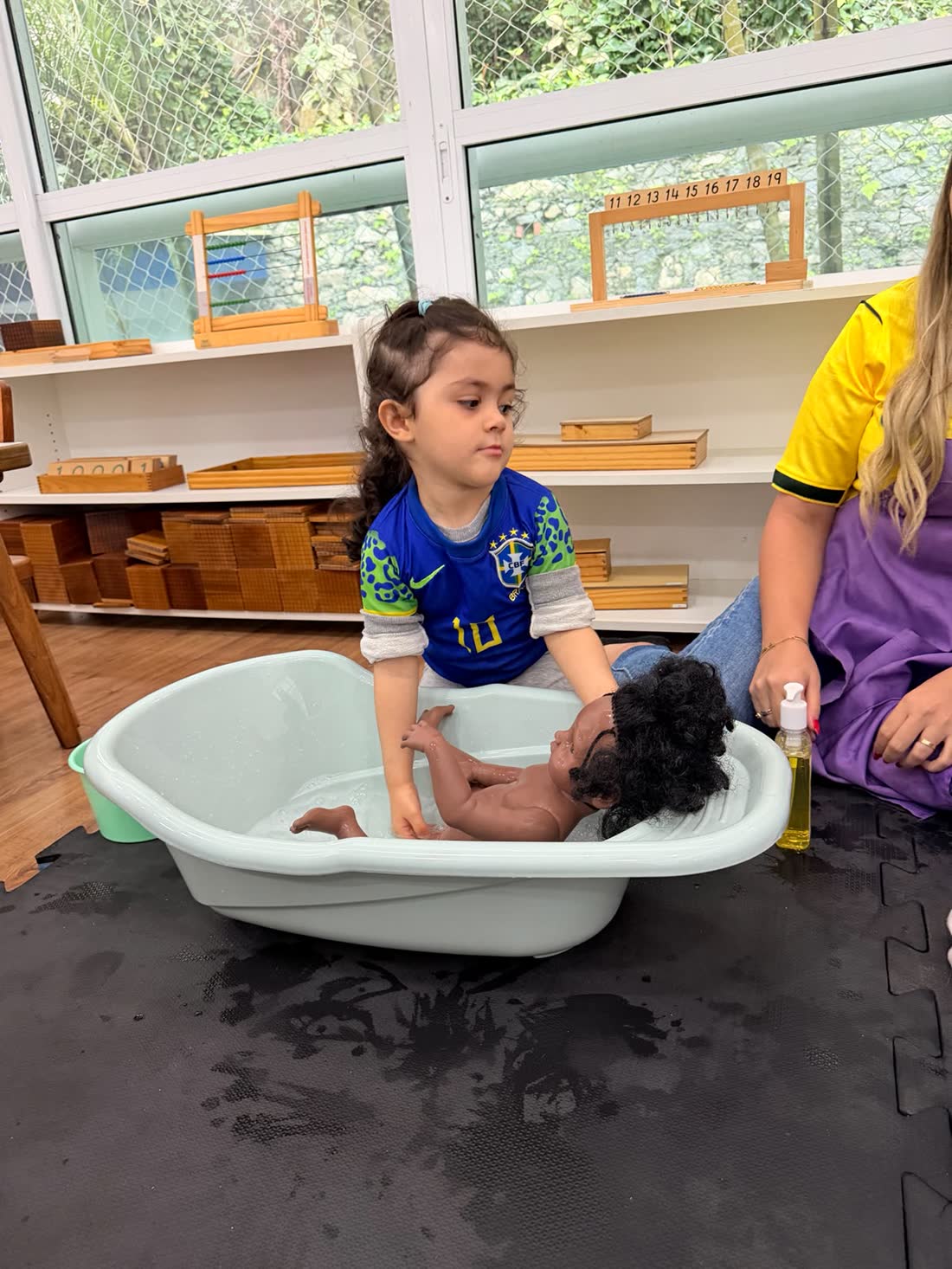 Criança dando banho em um bebê de brinquedo com cuidado, atividade Montessori de cuidado com o outro