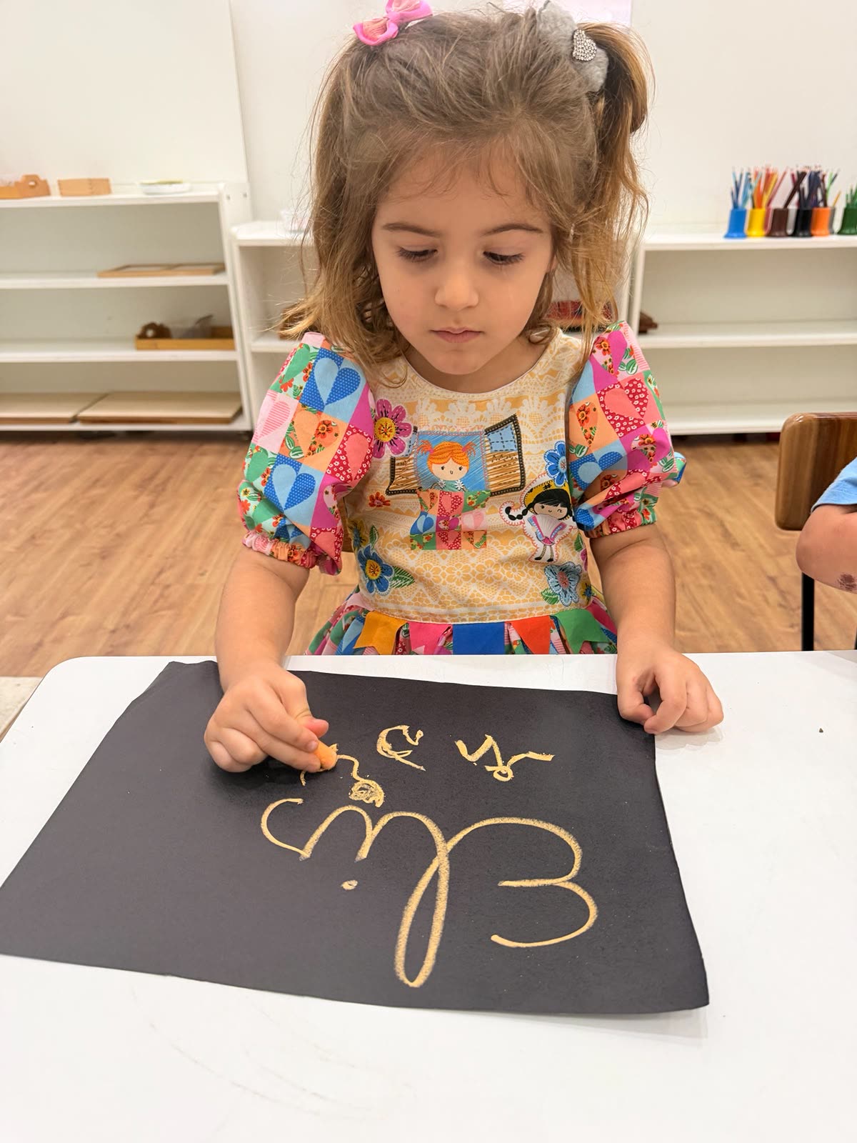 Criança concentrada escrevendo seu nome, atividade de linguagem Montessori