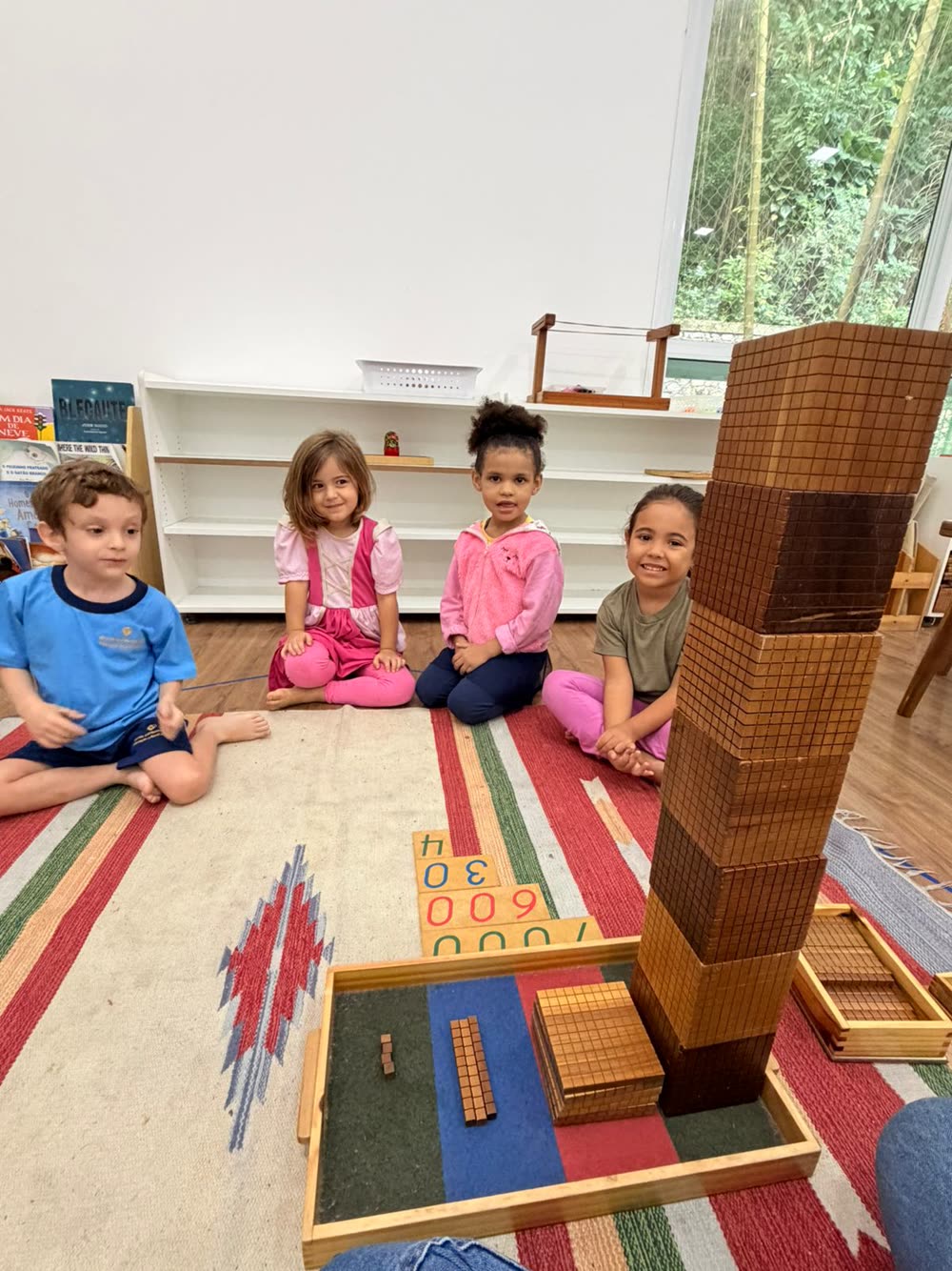 Crianças no tapete com a torre montada de Material Dourado e os cartões de números