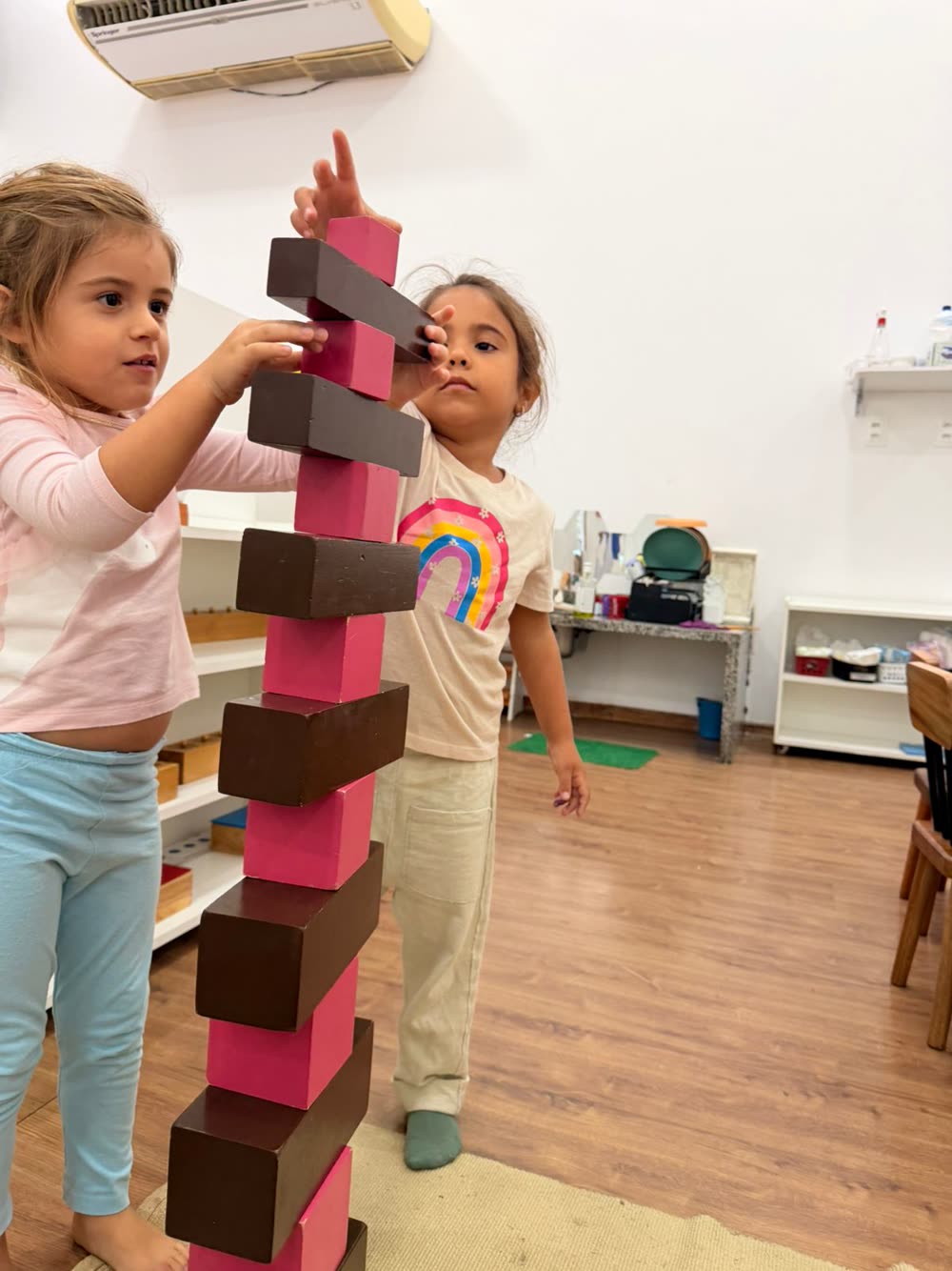 Criança concentrada montando a Torre Rosa, material Montessori clássico, na sala preparada