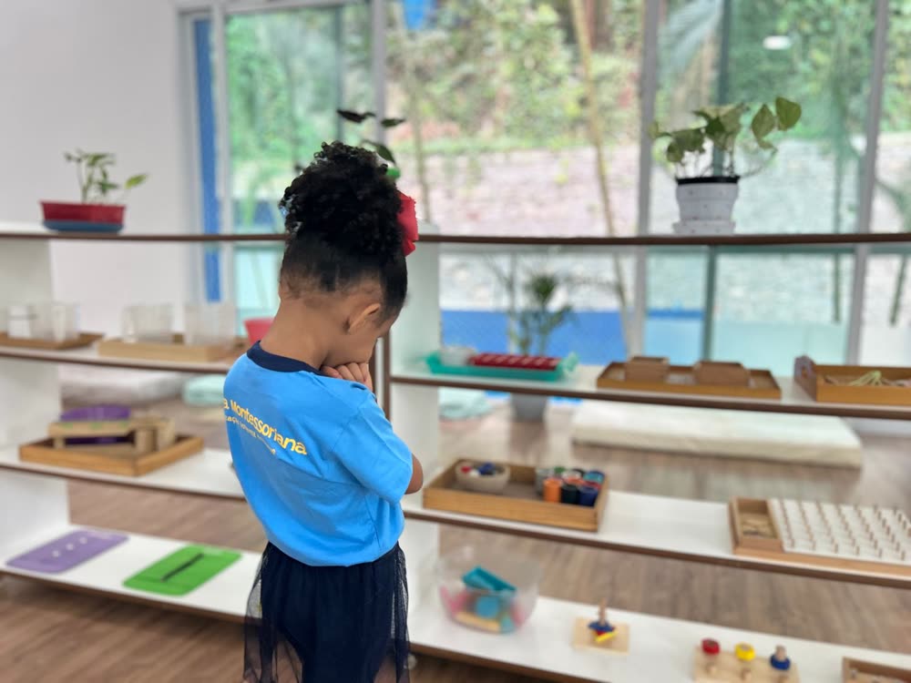 Criança pega seu trabalho sozinha na estante baixa de uma sala Montessori preparada
