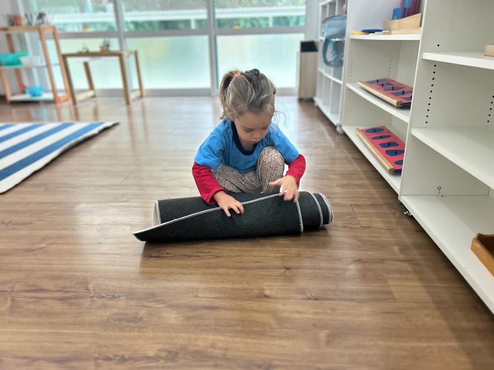 Criança enrolando o tapete sozinha ao terminar seu trabalho, na sala Montessori