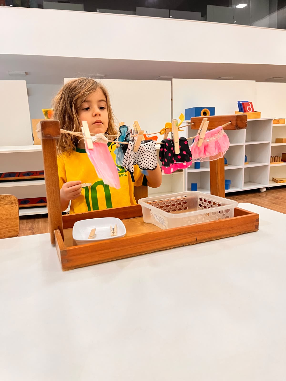 Criança pendurando roupas no varal com prendedores, atividade de Vida Prática Montessori