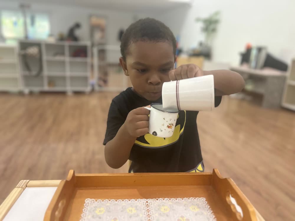 Menino concentrado versando líquido de uma caneca para a xícara, exercício de Vida Prática