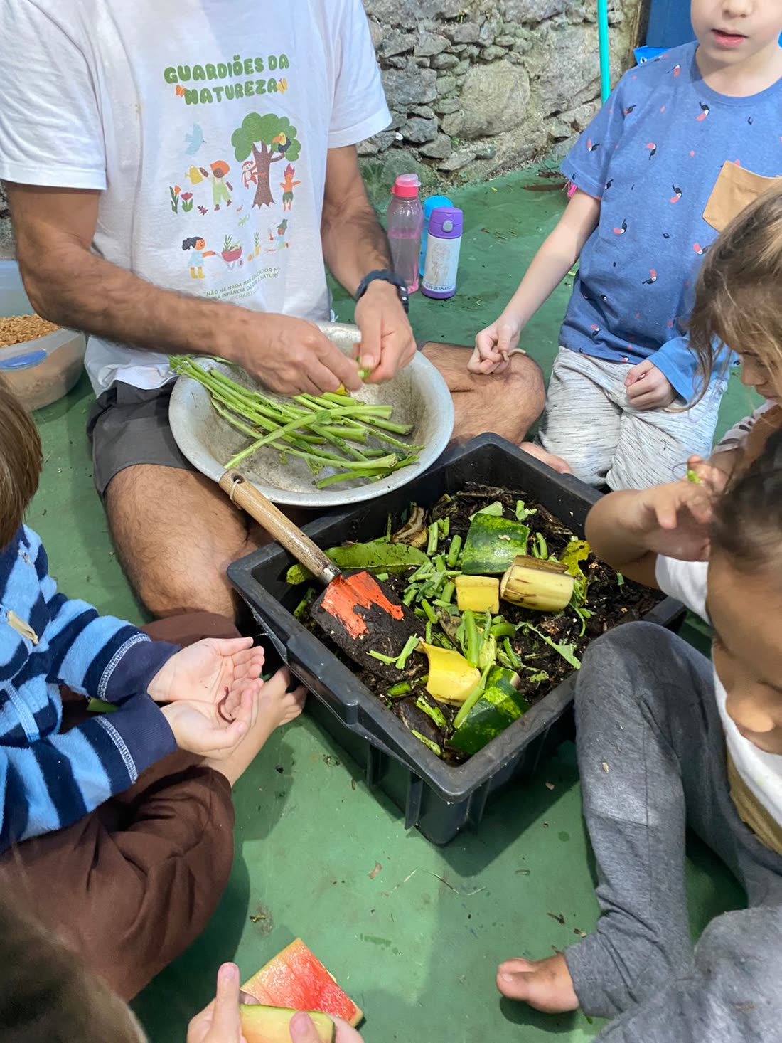Educador e crianças ao redor da caixa de compostagem com restos de frutas e verduras virando terra