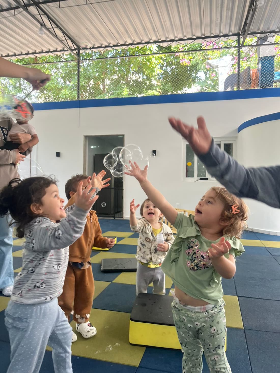 Crianças brincando com bolhas de sabão no pátio arborizado